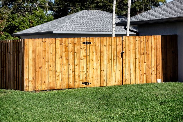 Wooden fence with a gray shingled roof behind it and green grass in front
