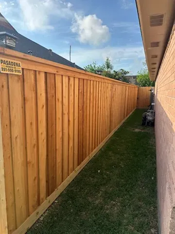 Wooden privacy fence along a narrow grassy side yard beside a house under a partly cloudy sky