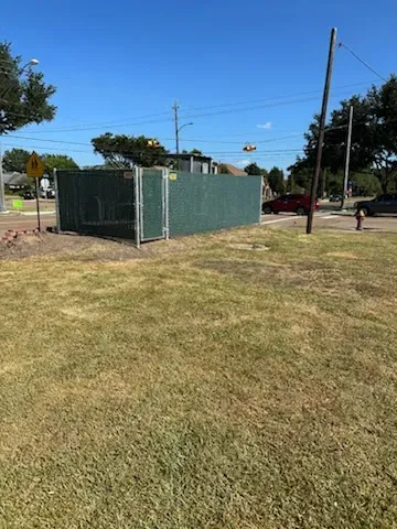 Green fenced utility enclosure on a grassy roadside under a clear blue sky.