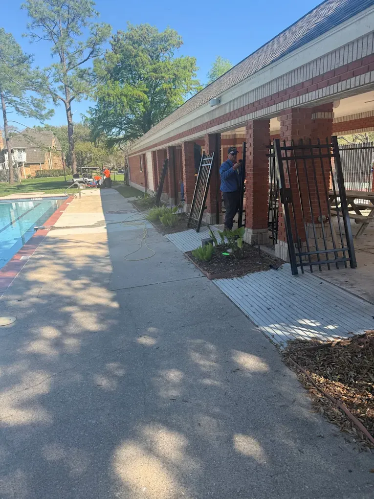 Poolside walkway beside brick apartments with a person standing near a doorway on a sunny day