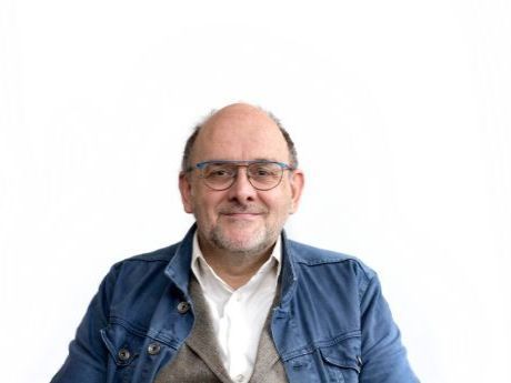 Man wearing glasses and a blue jacket, smiling against a white background