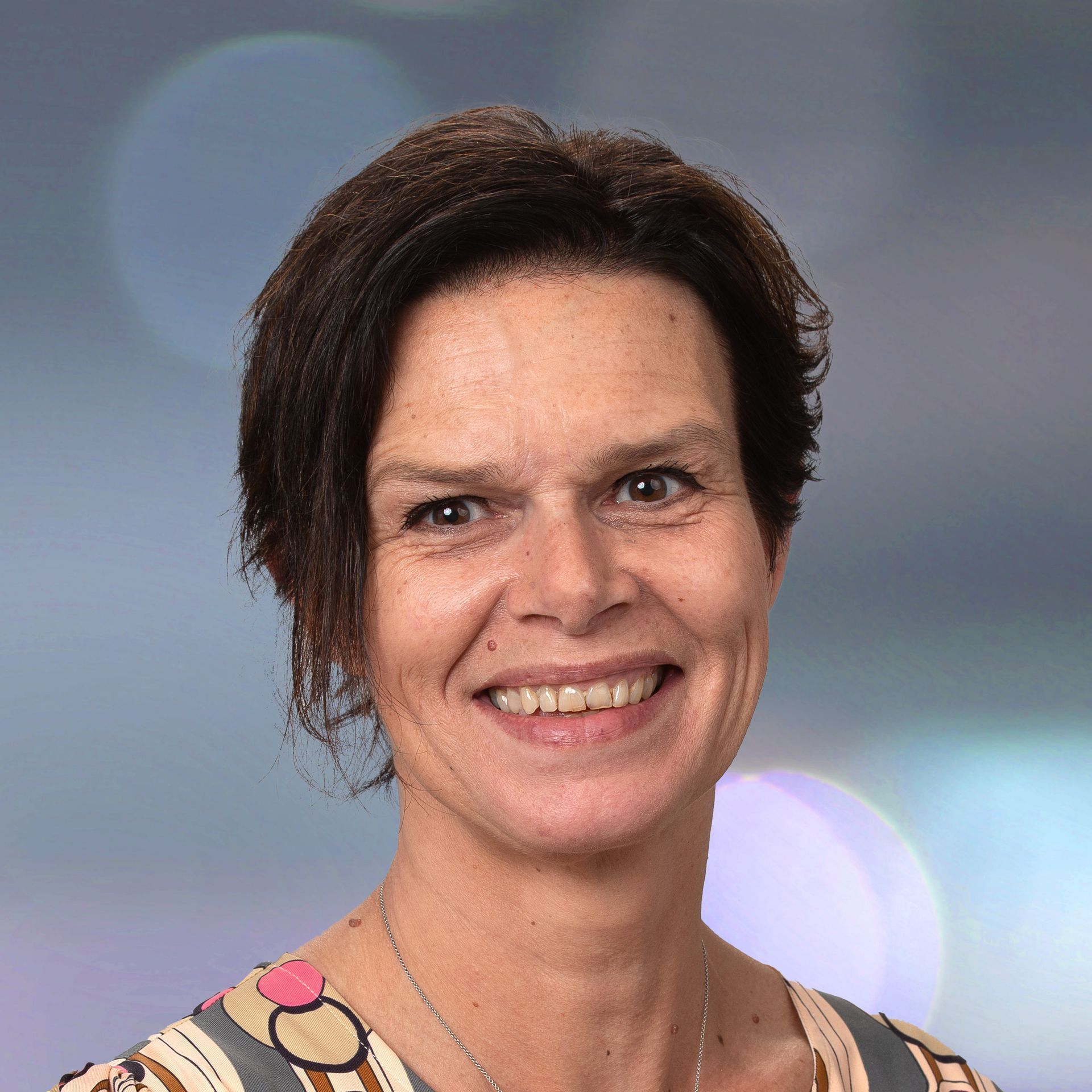 Smiling person with short dark hair against a softly blurred blue background