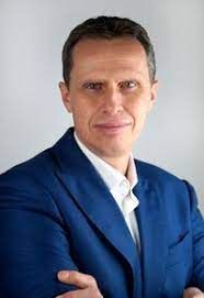 Portrait of a man in a blue suit with arms crossed against a light gray background