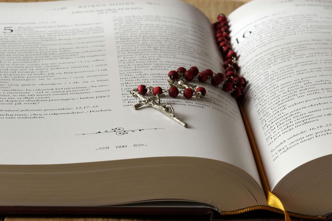 Open book with red rosary beads and a crucifix lying across the pages