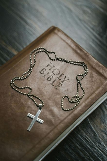 Brown Bible with a rosary and silver cross on a wooden surface, titled “HOLY BIBLE.”