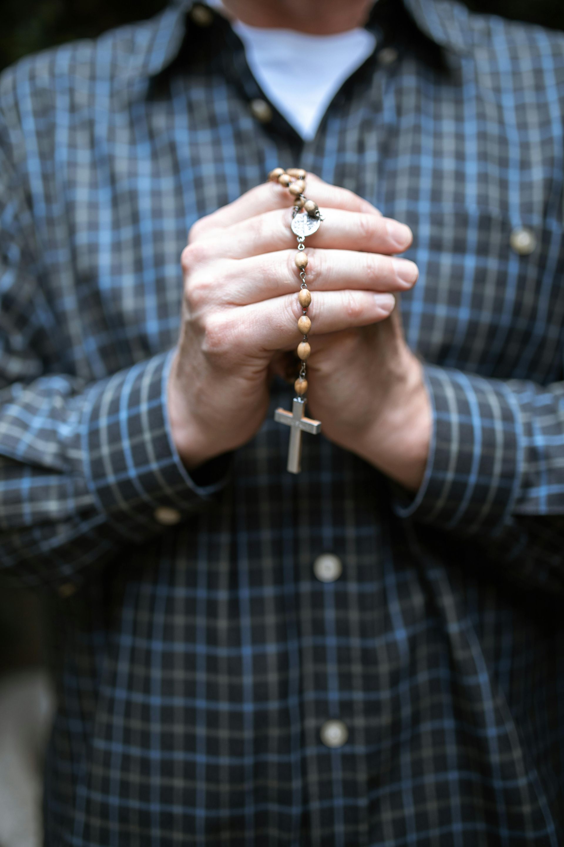 Hands holding a rosary with a cross pendant against a blue plaid shirt