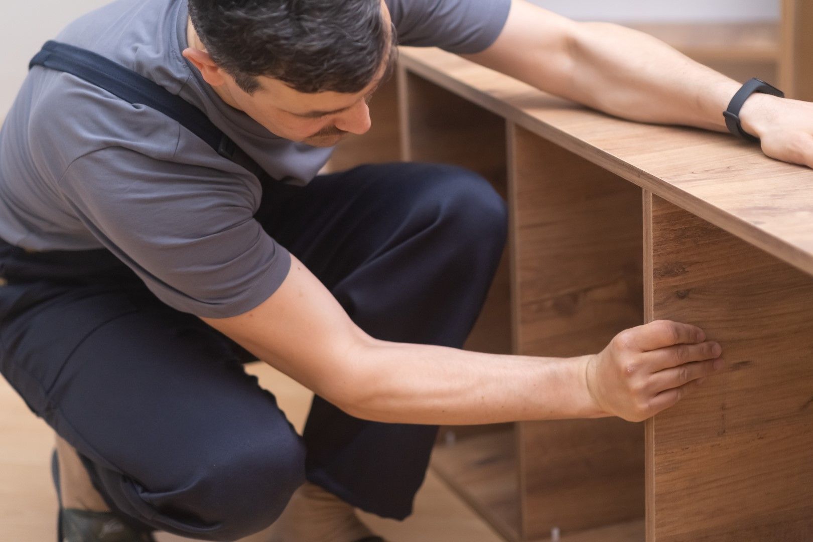 Man assembling a wooden cabinet, kneeling and inspecting the frame.