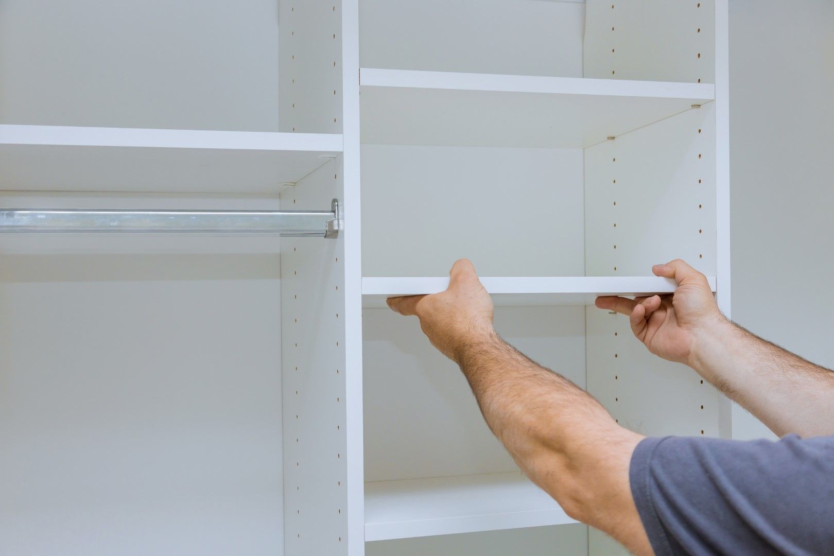Person installing a white shelf in a closet.