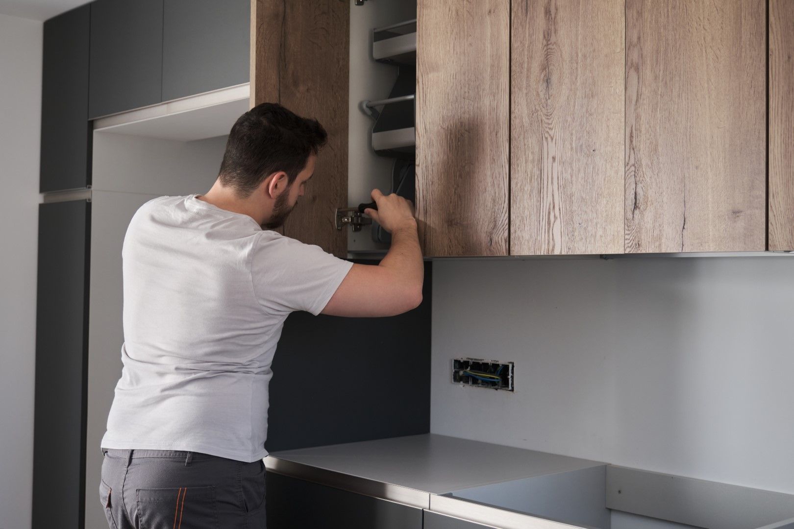 Man installing a kitchen cabinet; wood and gray tones, light gray counter.