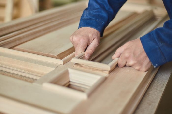 Hands assembling wooden door components on a workbench.