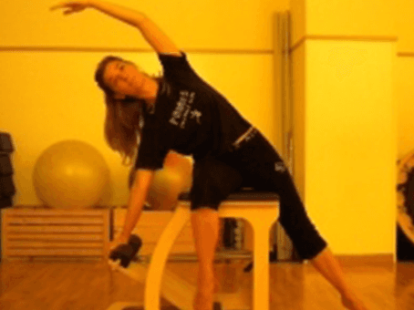 Una persona in abbigliamento sportivo nero si allunga lateralmente in una palestra con una palla da ginnastica gialla.