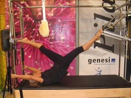 Una persona al trapezio esegue una spaccata in palestra, con una corda e un tappetino sospesi sotto.