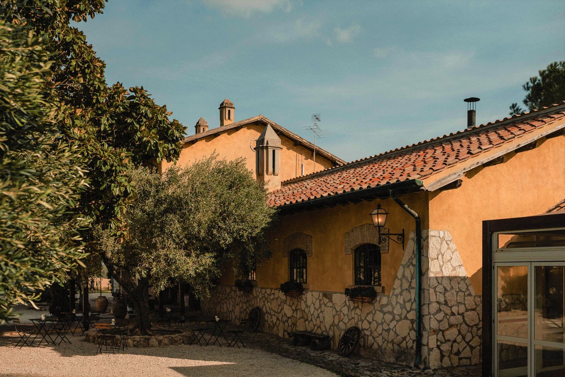 Edifici gialli con tetti di tegole rosse sotto un cielo azzurro, alberi in primo piano.