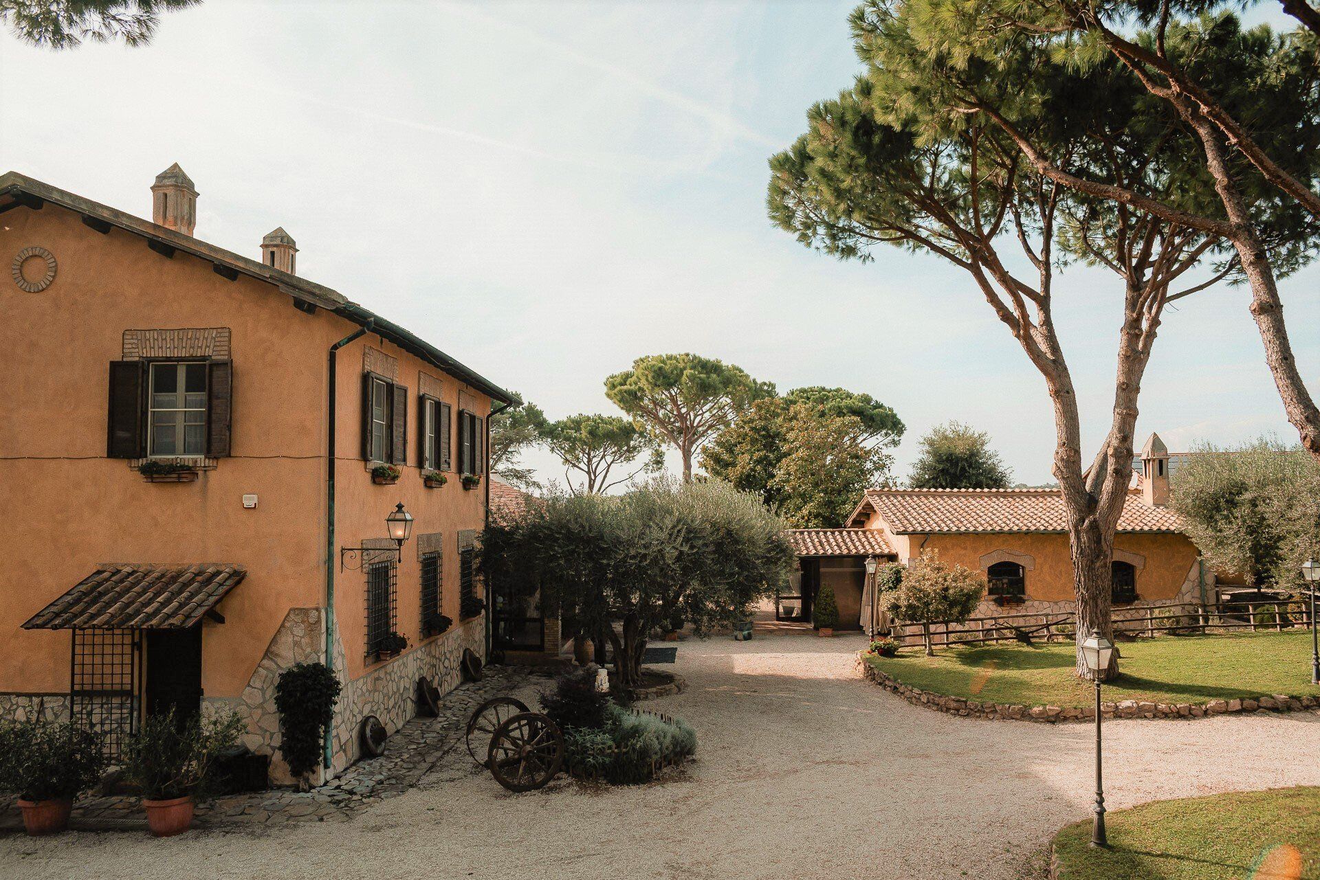 Villa italiana gialla con tetto in tegole rosse, vialetto di ghiaia, alberi e cielo azzurro.