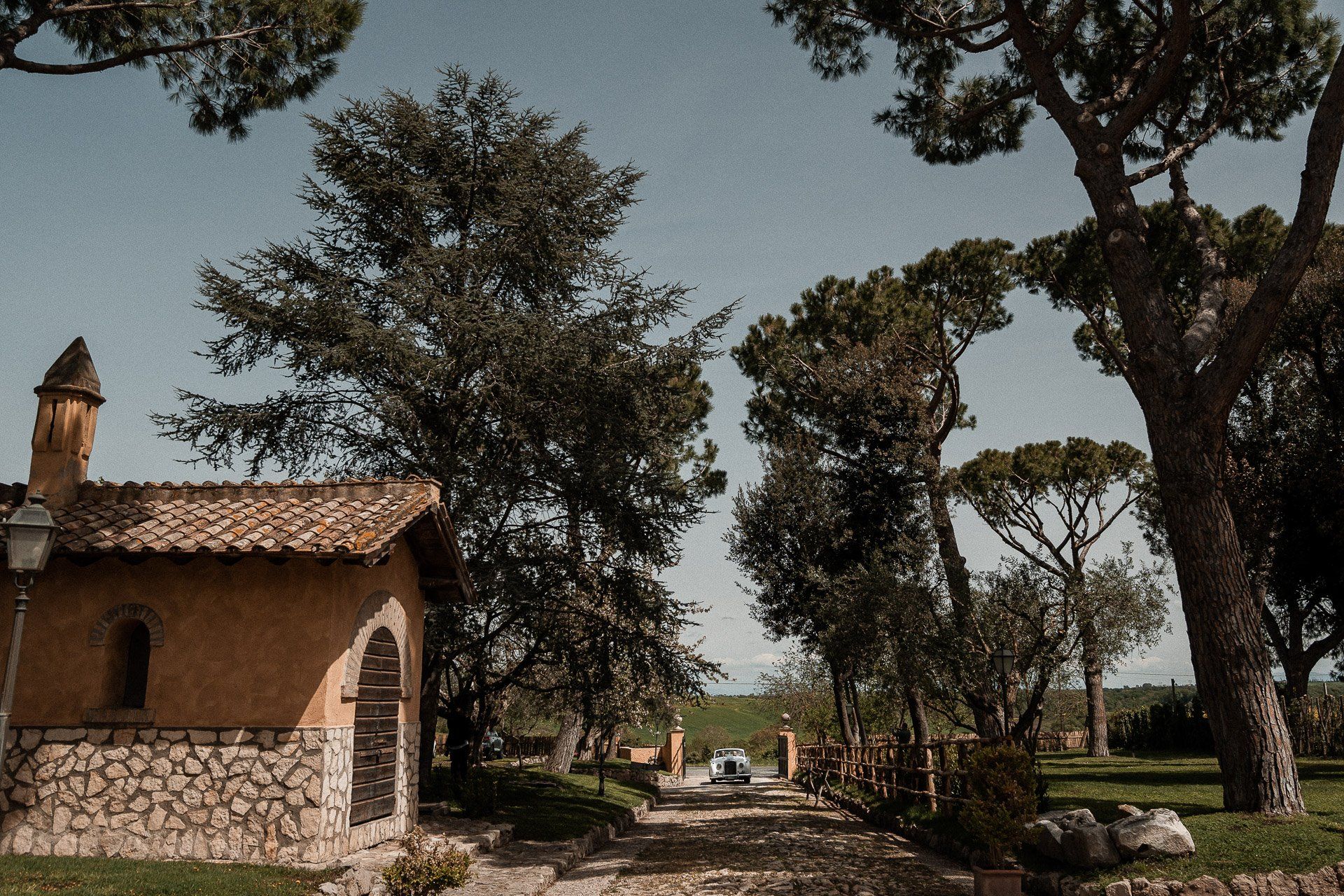 Piccolo edificio in pietra color marrone chiaro con tetto di tegole, alberi e un sentiero nelle giornate di sole.