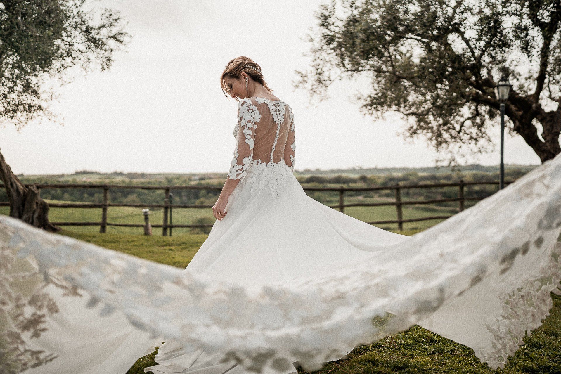Sposa in abito da sposa bianco con dettagli in pizzo, con strascico fluente all'esterno.