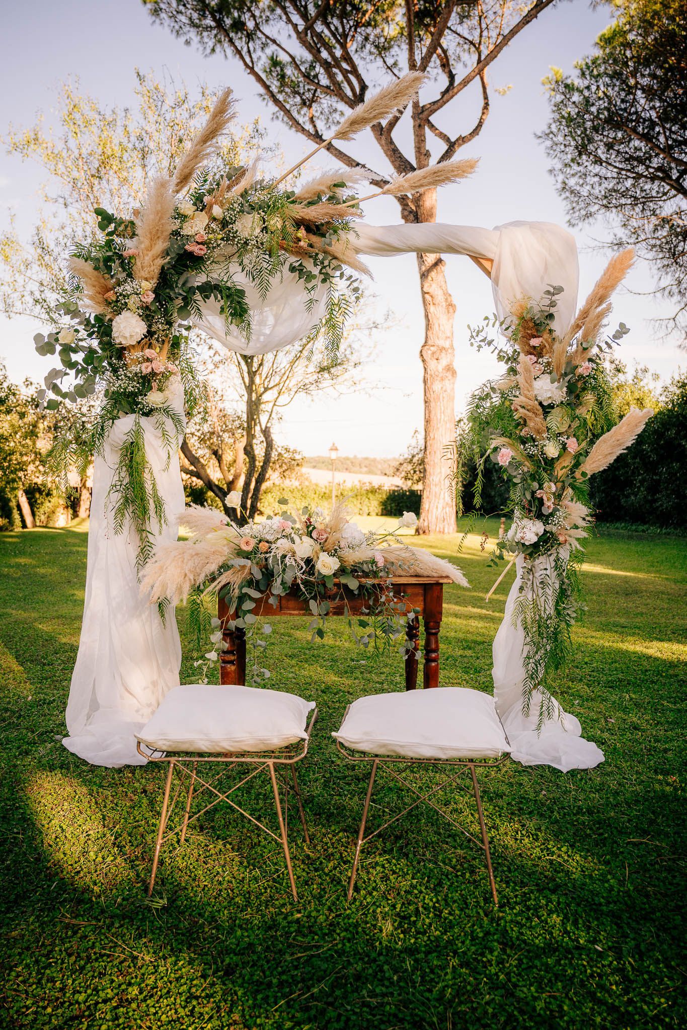 Arco nuziale decorato con fiori e stoffa, situato in un giardino con sedie.