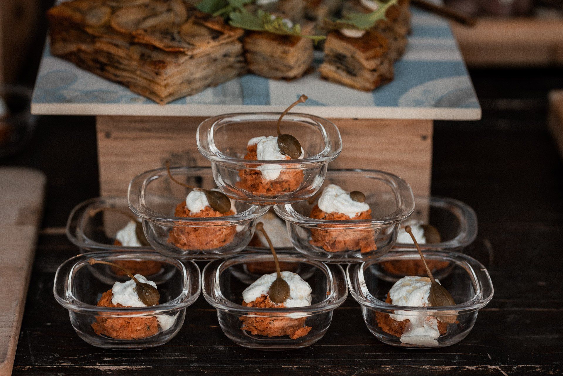 Antipasti in ciotole di vetro, impilati a piramide, guarniti con panna e capperi.