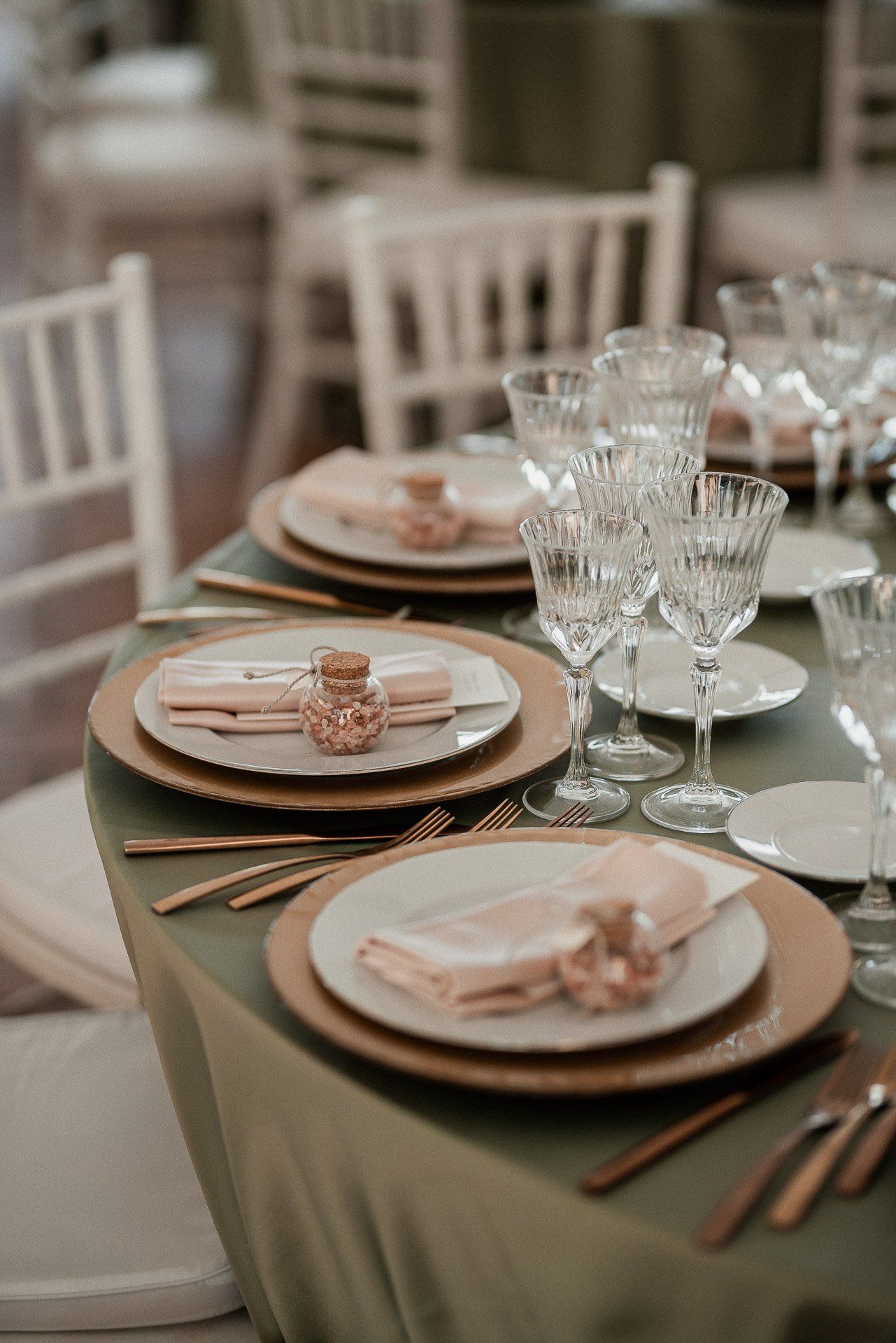 Elegante apparecchiatura da tavola con sottopiatto dorato, piatti bianchi, bicchieri di cristallo e tovaglioli piegati su una tovaglia verde.