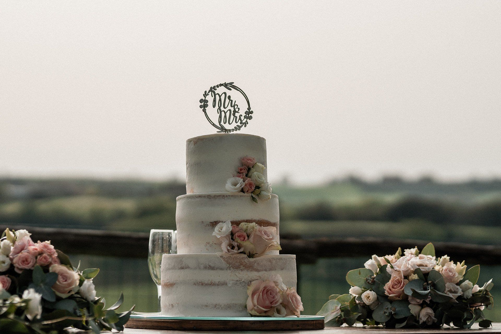 Torta nuziale a tre piani con decorazioni floreali e topper con la scritta