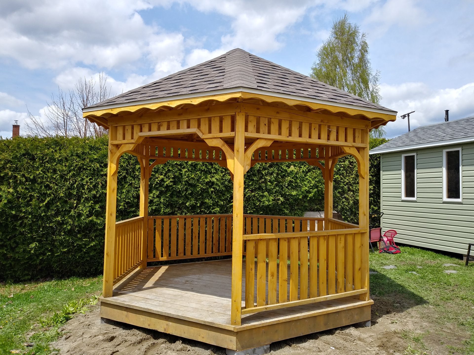 Gazebo en bois au toit marron, dans une cour gazonnée.