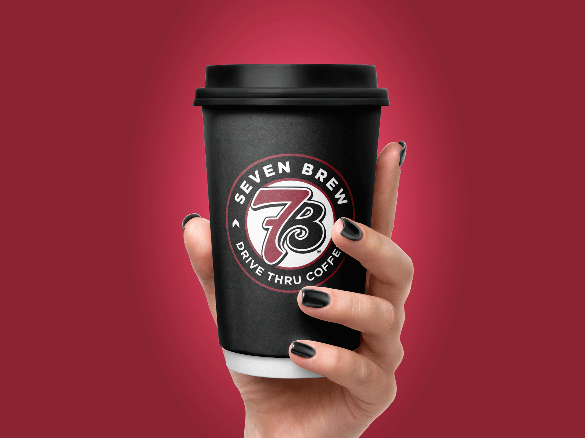 Hand holding a black Seven Brew coffee cup with white lid against a red background by Existence Creative