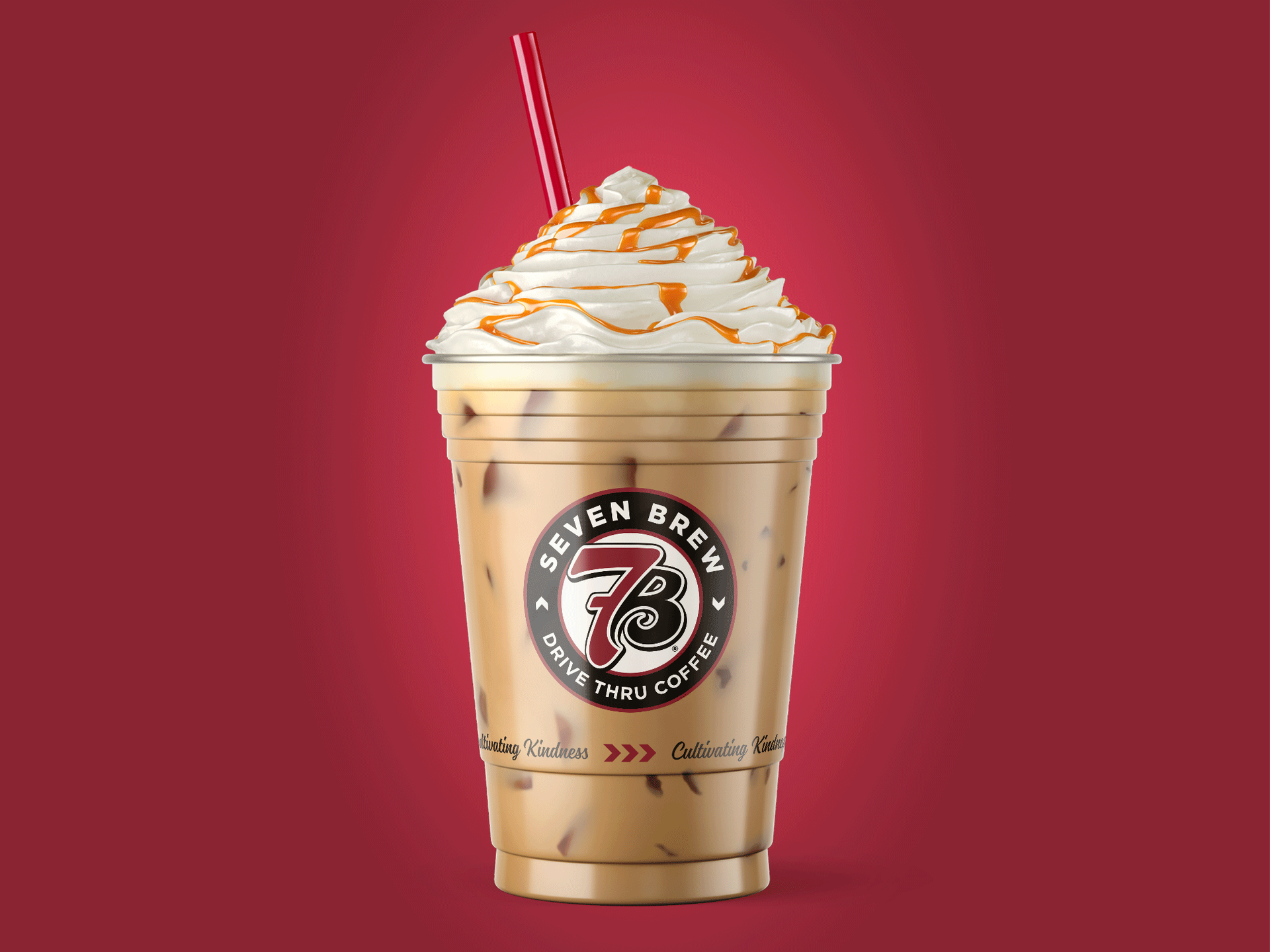 Iced coffee with whipped cream and caramel drizzle in a clear cup with a straw on a red background by Existence Creative