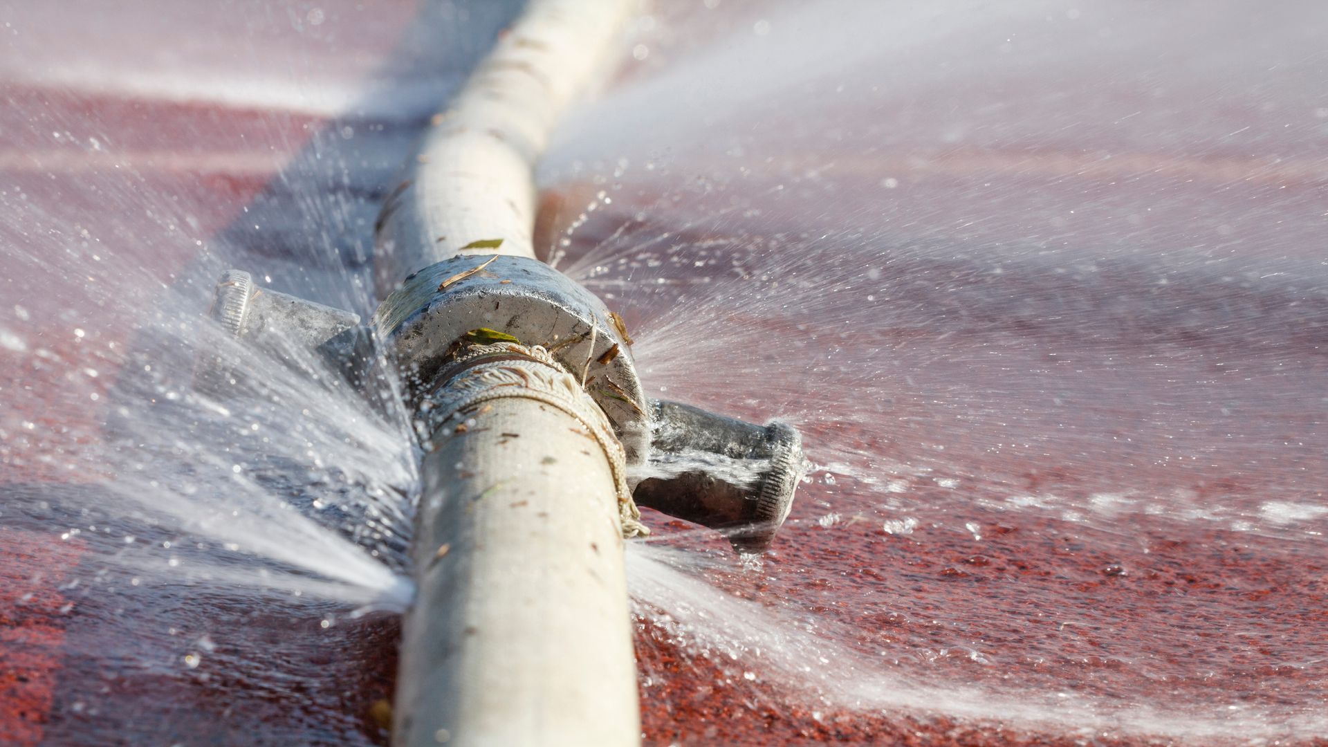 White pipe spraying water across a wet red surface outdoors.