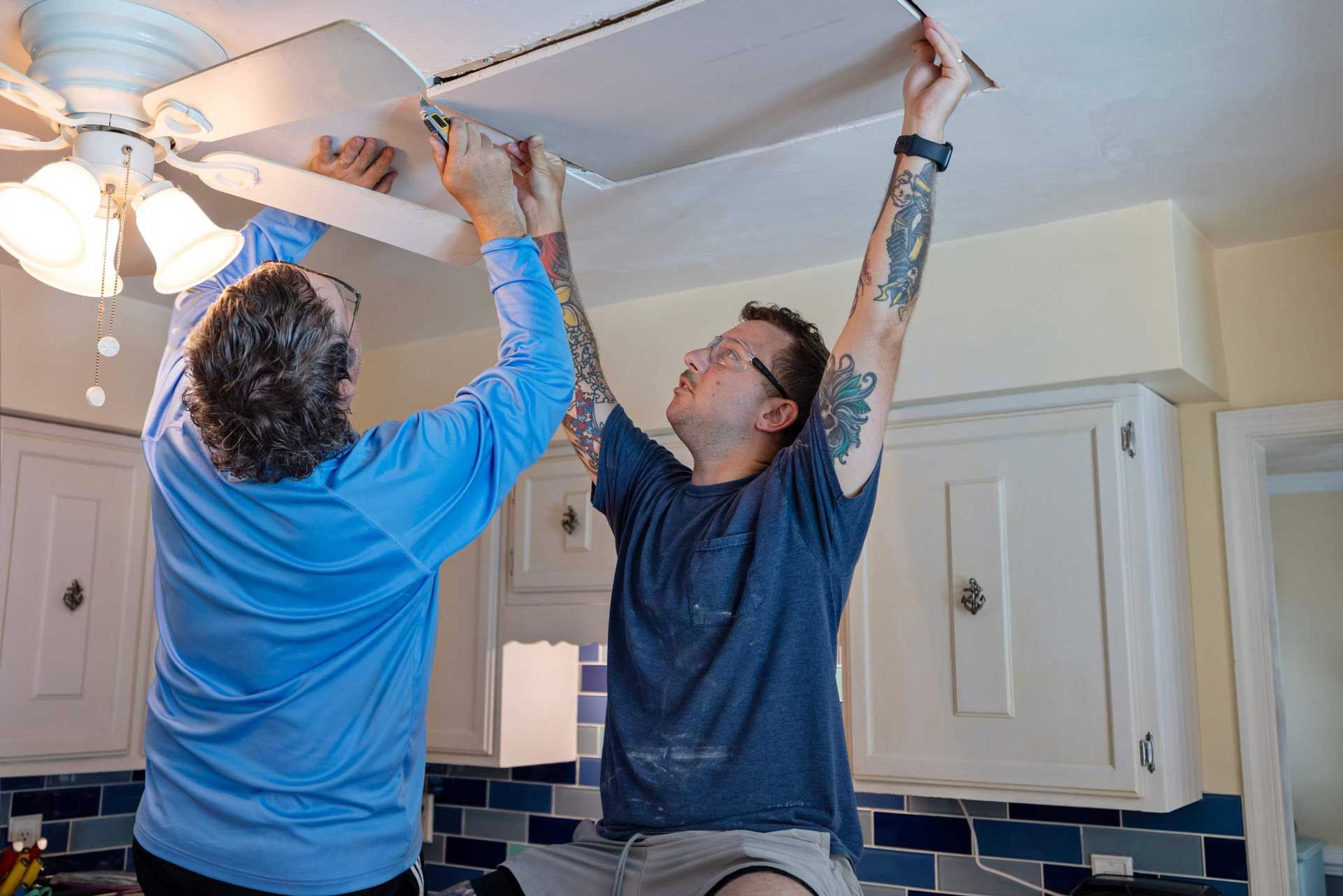 Two people installing a ceiling light fixture in a kitchen.