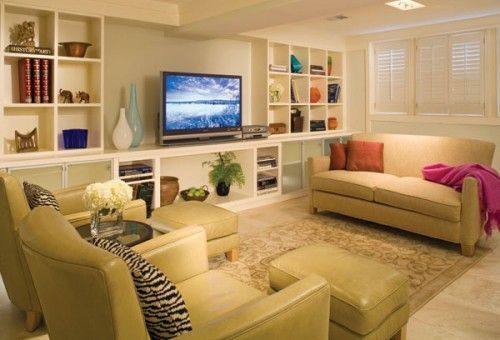 A living room filled with furniture and a flat screen tv Living room with built-in shelves, sofa, chairs, ottomans, and a TV. Beige and cream color scheme.