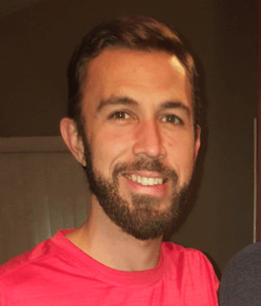 A man with a beard is wearing a red shirt and smiling