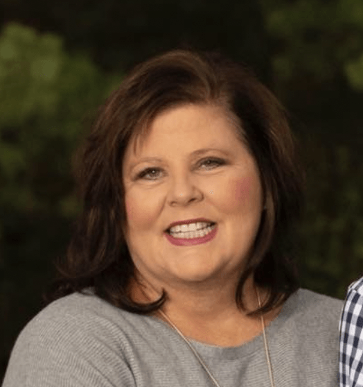 A woman in a grey shirt is smiling for the camera.