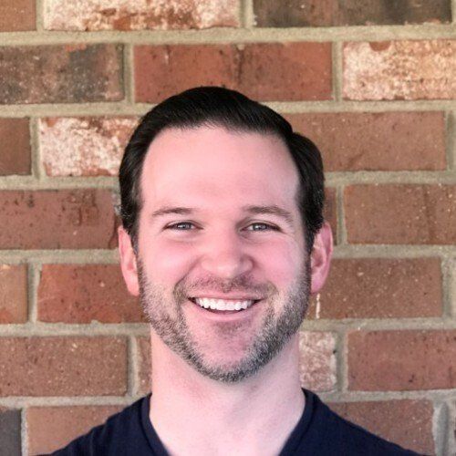 A man with a beard is smiling in front of a brick wall.