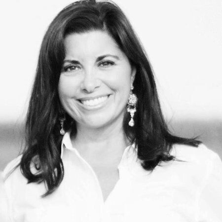 A woman wearing a white shirt and earrings is smiling in a black and white photo.
