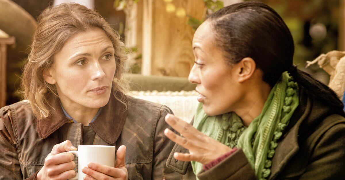 Two women are sitting at a table drinking coffee and talking to each other.