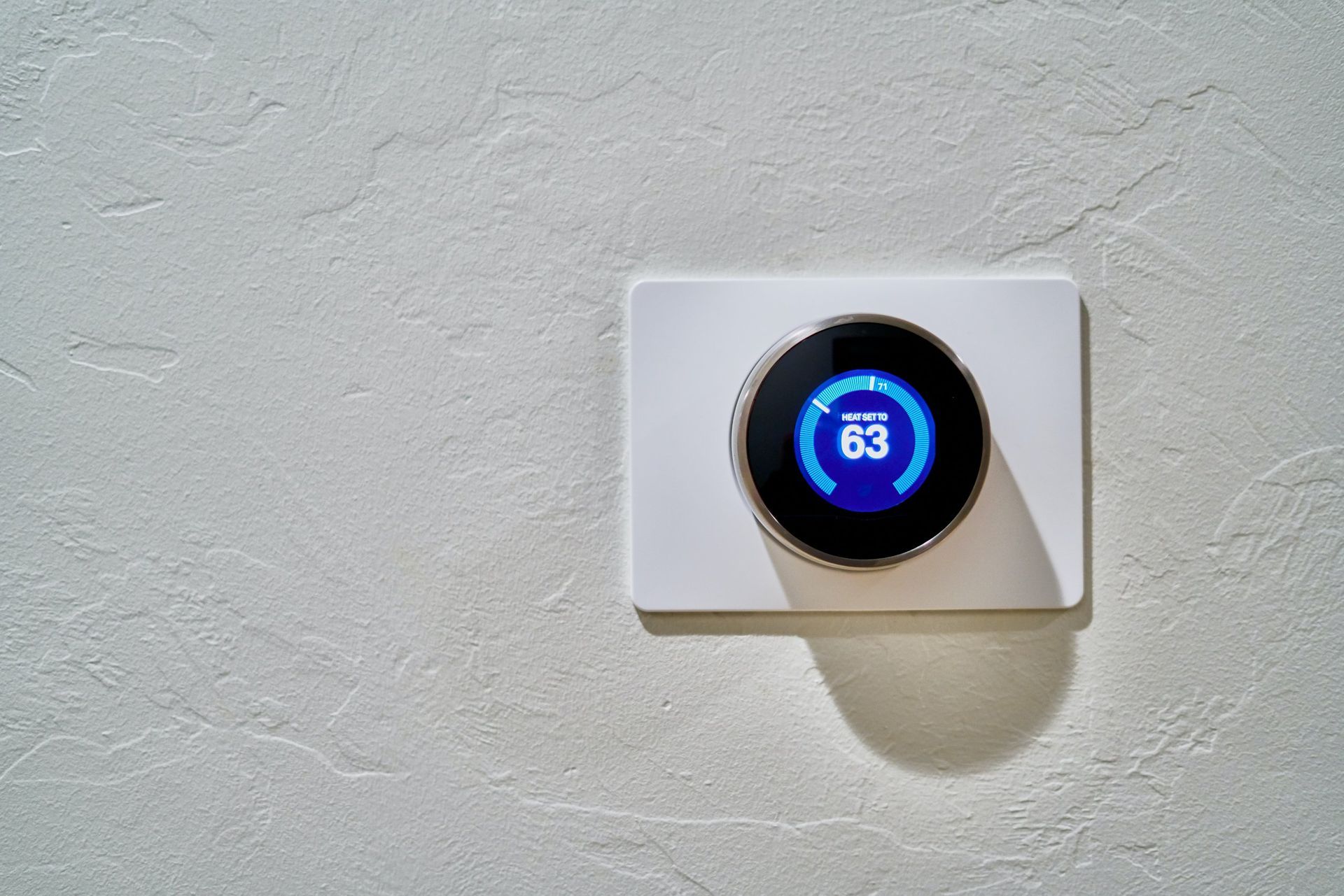 A smart thermostat is hanging on a white wall.