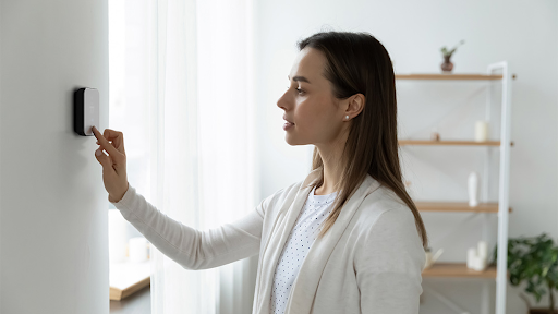 A woman is adjusting a thermostat in a living room.