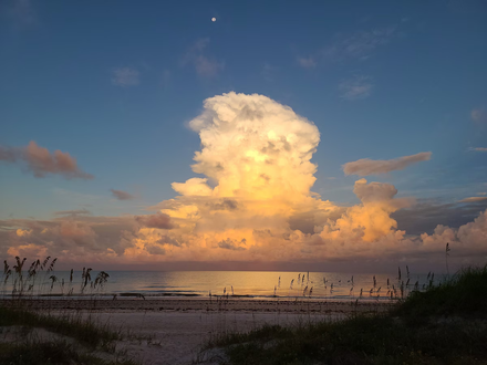 Sunset over calm beach with a towering golden cloud and blue sky