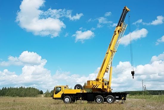 Una gru gialla è seduta in cima a un camion in un campo.