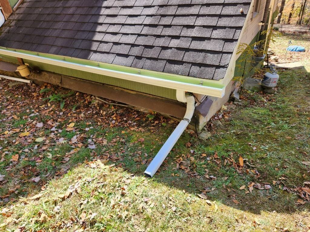 A gutter on the side of a house next to a roof.