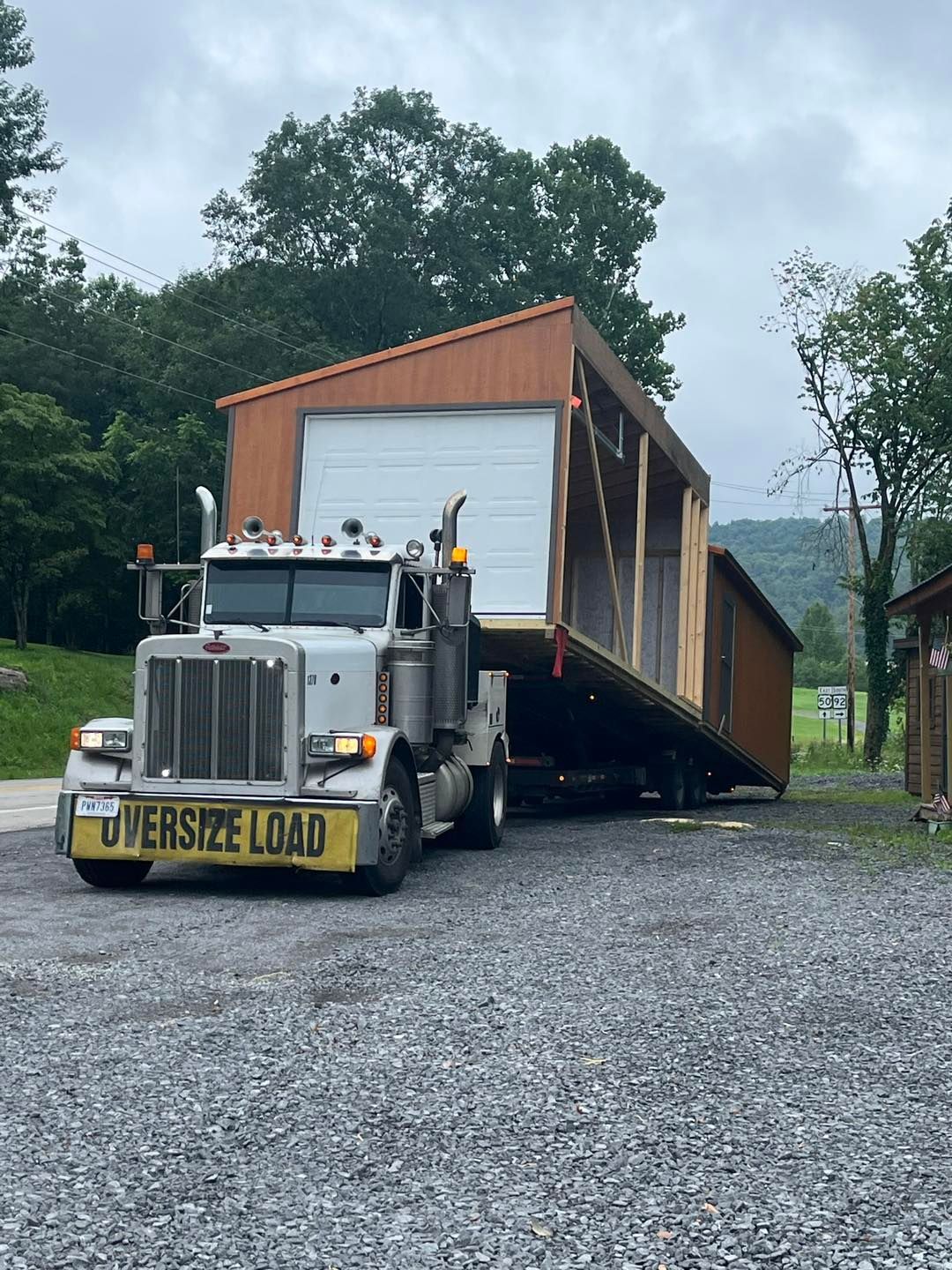 A semi truck is carrying a shed on a gravel road.