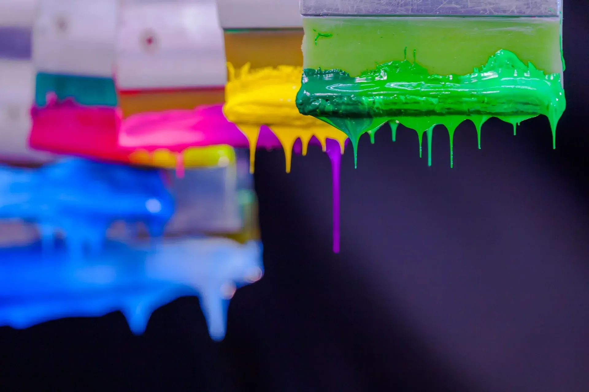 A close up of a squeegee with colorful paint dripping from it.