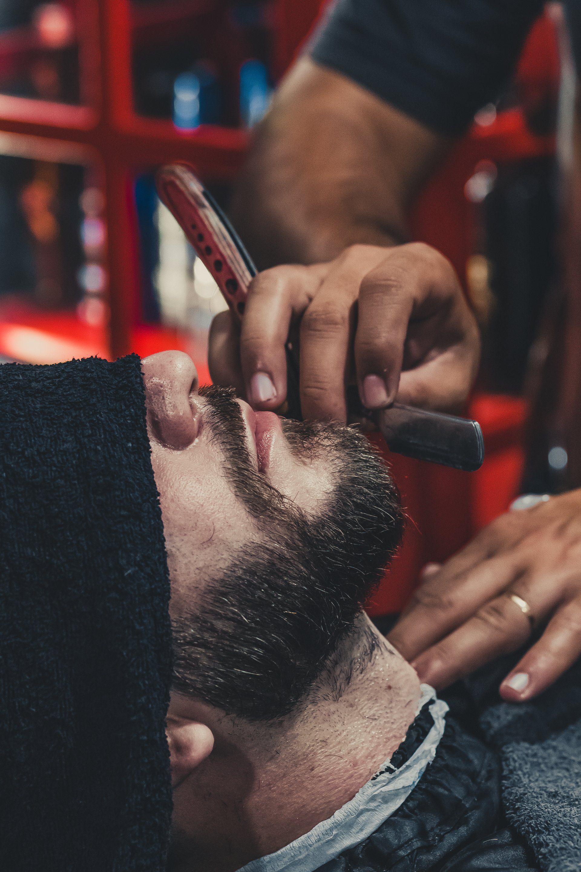 A man is getting his beard shaved by a barber with a razor.