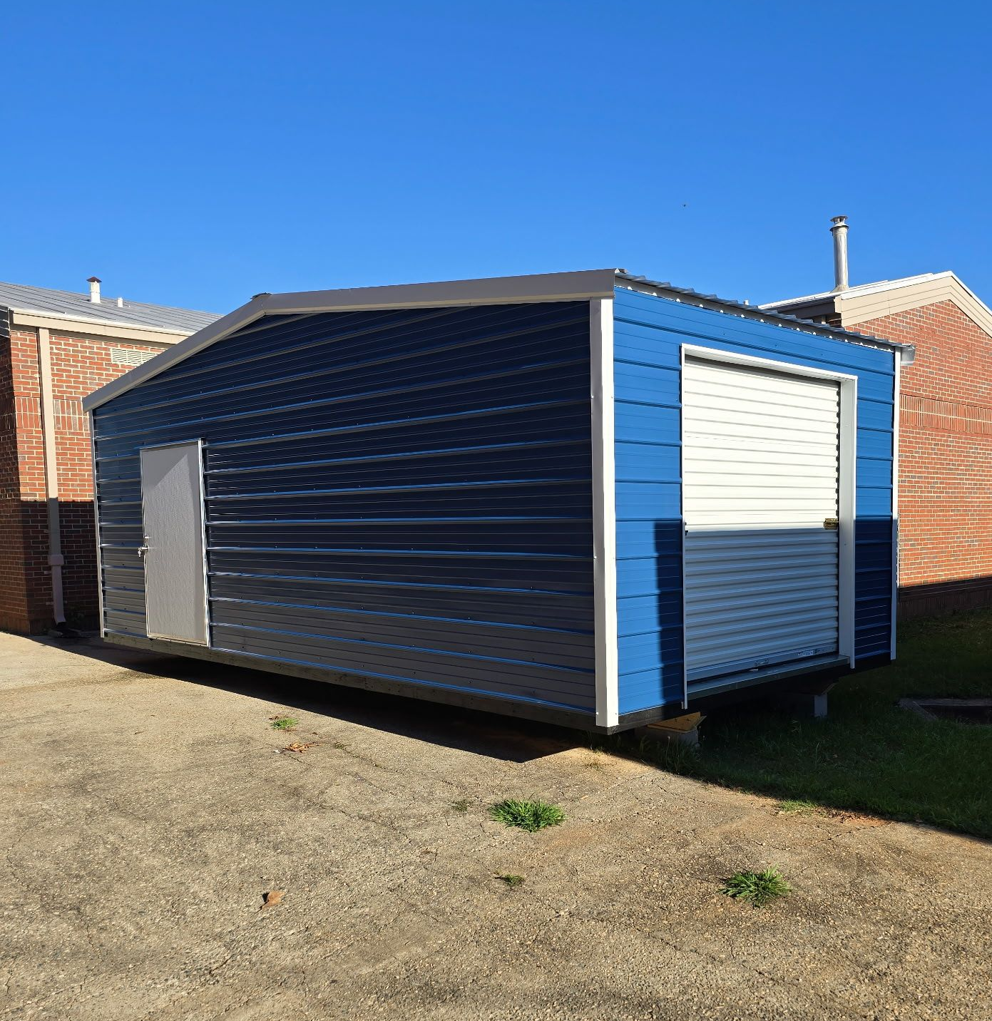 Blue-and-white shed on gravel beside brick buildings under a clear sky