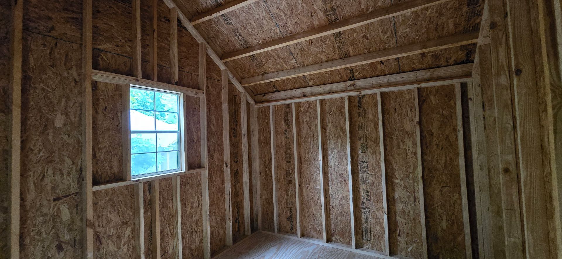 Empty unfinished wooden room with exposed studs, sloped ceiling, and a small window