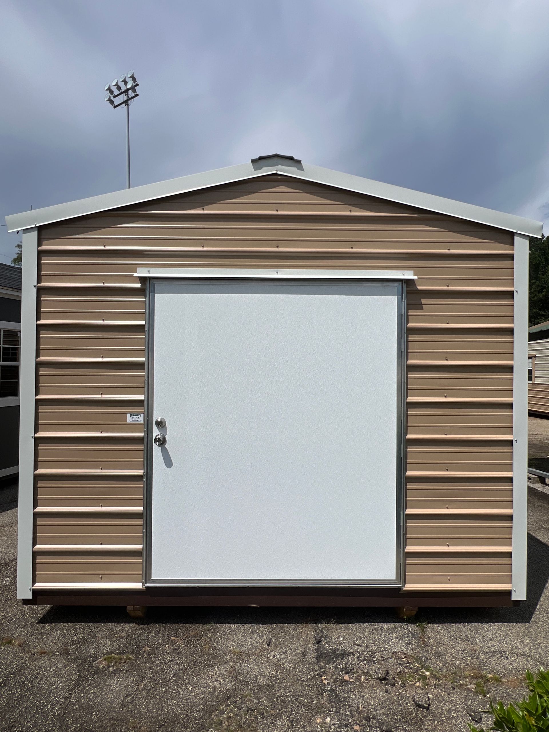 Small tan shed with a white door, centered on gravel under a cloudy sky.