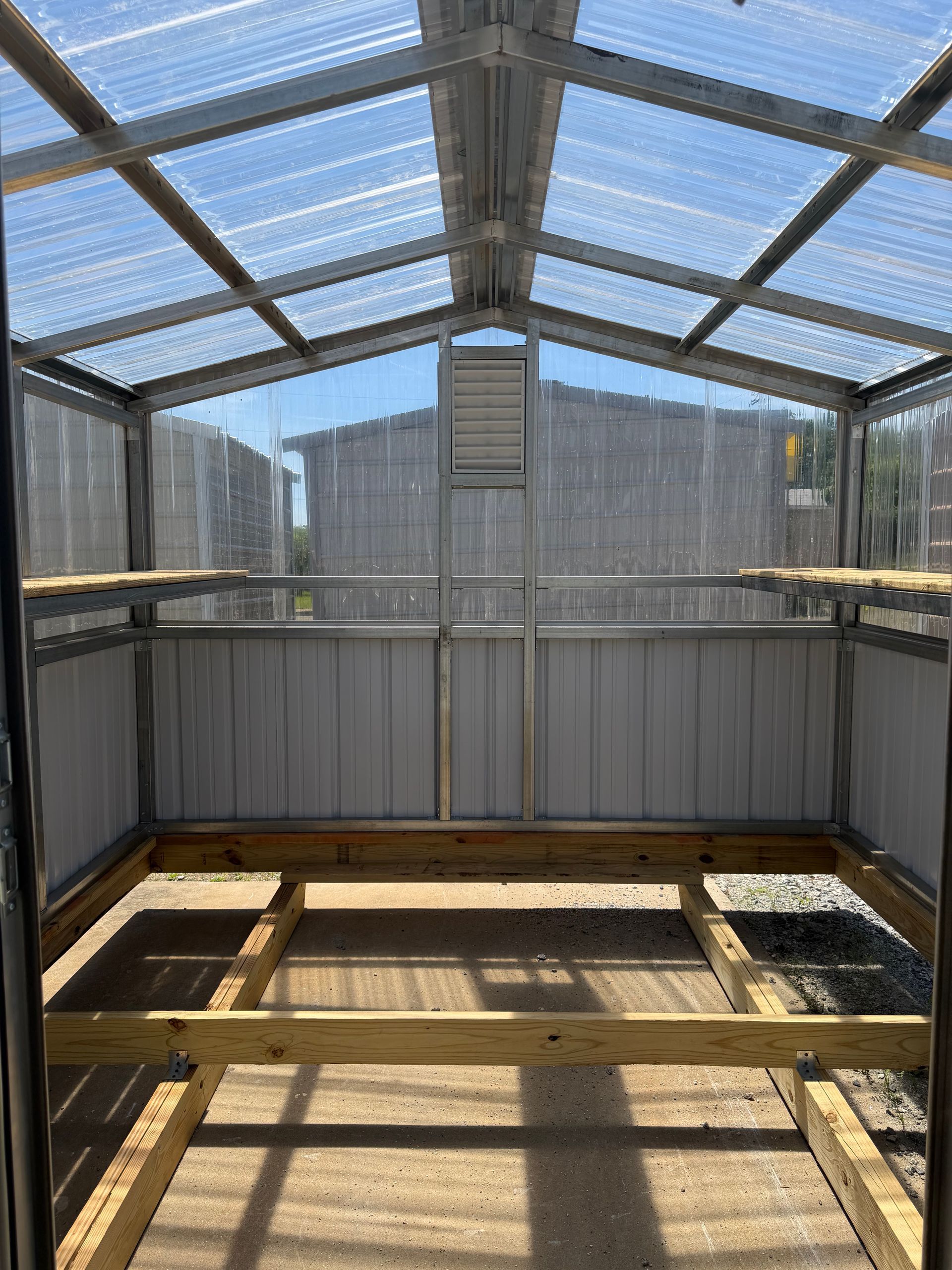 Empty greenhouse with clear roof panels, wooden frame, and sunlight casting shadows on the floor