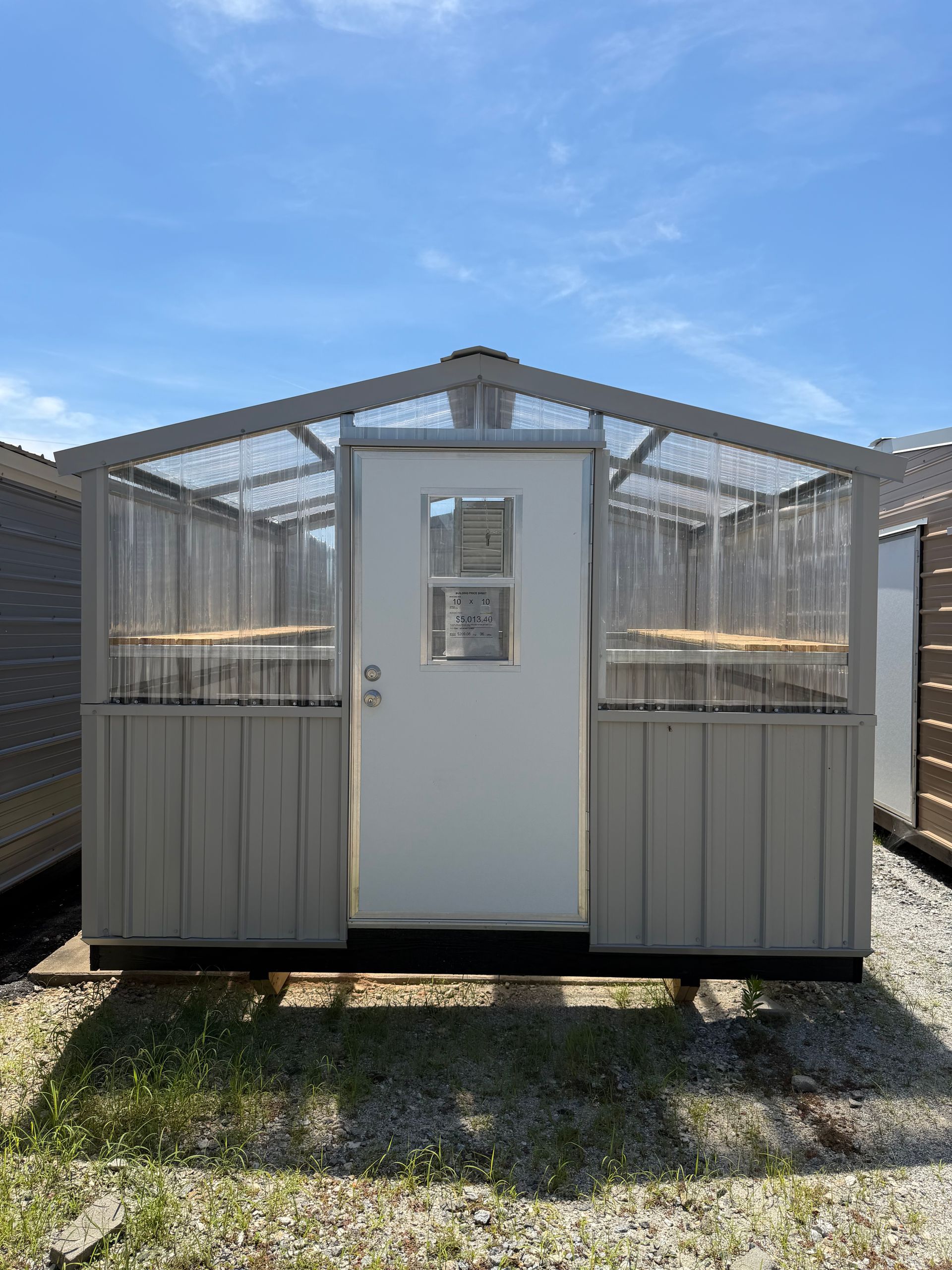 Small white greenhouse shed with clear roof panels on a grassy lawn under blue sky