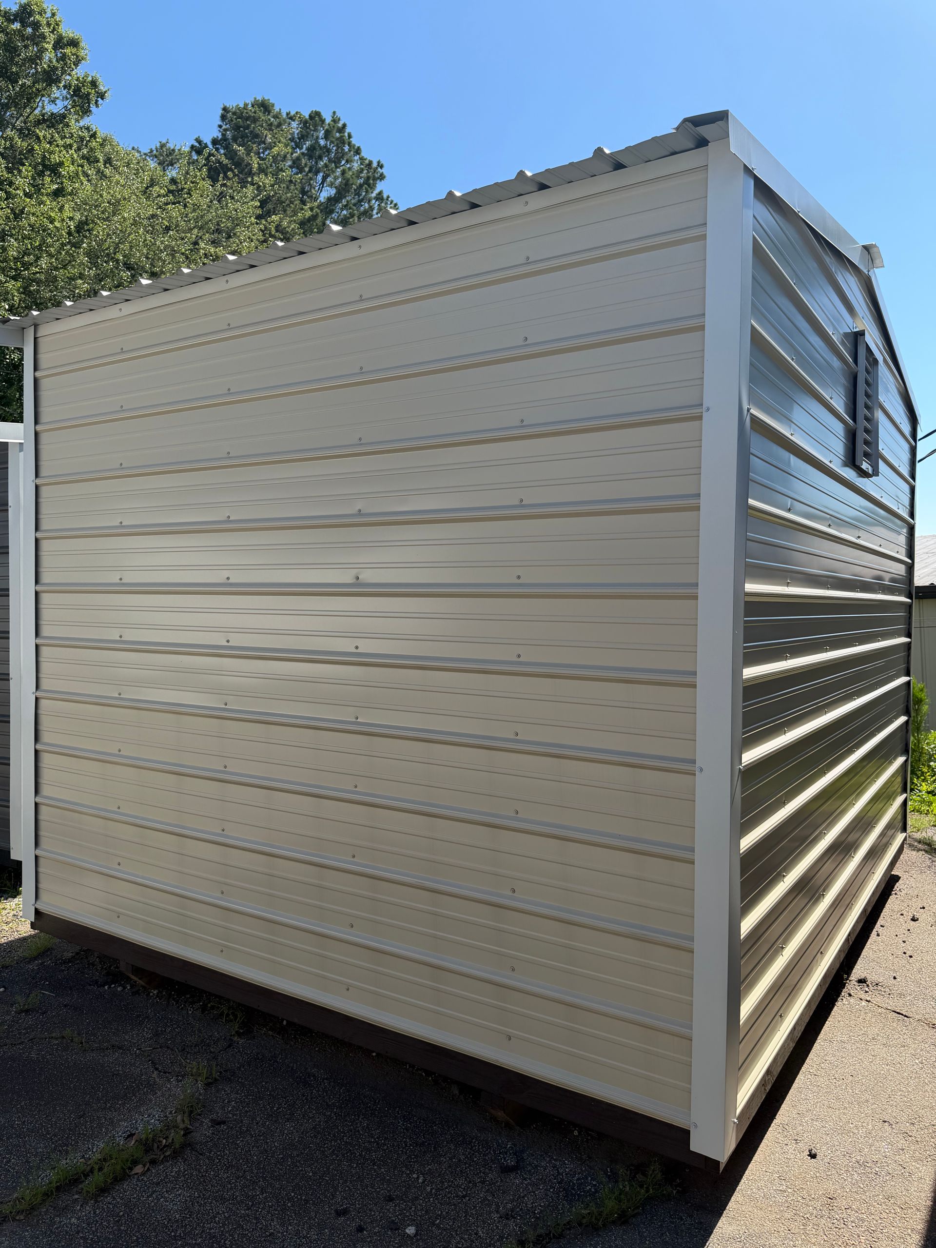 White metal storage shed with ribbed siding sitting on gravel outdoors in sunlight