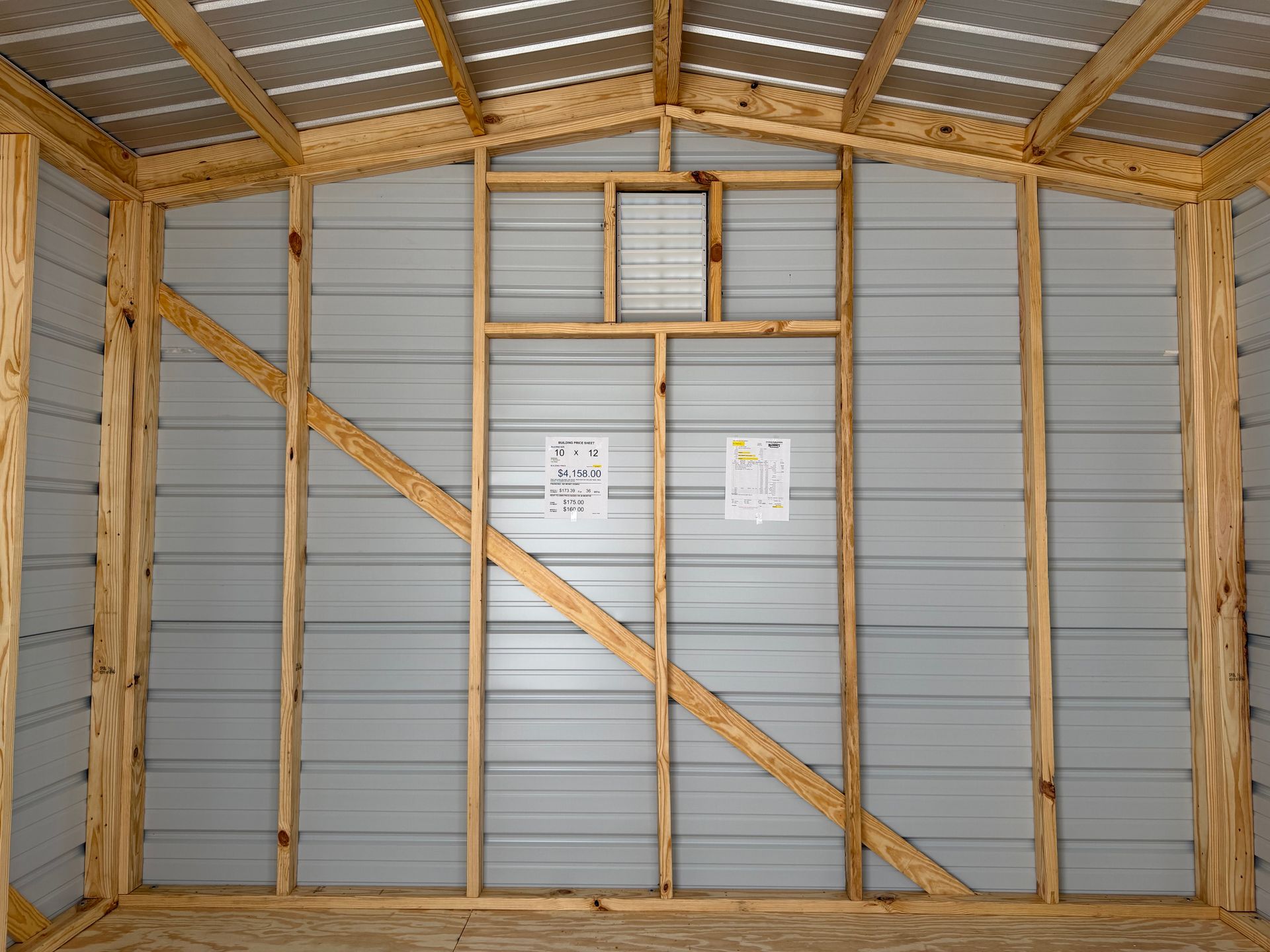 Interior of a wooden-framed shed under construction with gray metal wall panels and diagonal bracing.